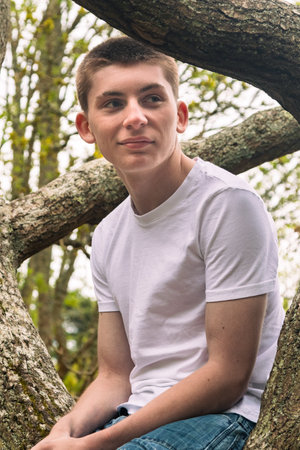 A teenage boy sitting in a tree in a public park, wearing a white t-shirt and blue denimの写真素材