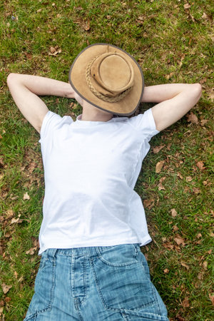 A teenage boy napping on grass, on a spring day with a bush hat covering his faceの写真素材