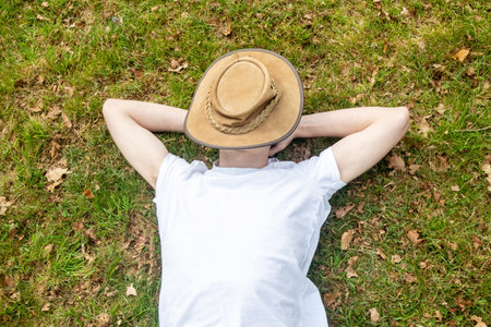 A teenage boy napping on grass, on a spring day with a bush hat covering his faceの写真素材