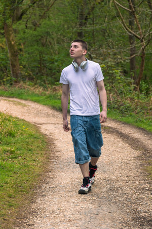 Teenage boy wearing a white t-shirt and blue denim, walking outside in a public parkの写真素材