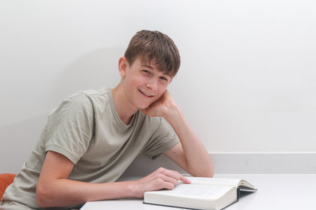 Teenage boy reading a novel at a desk