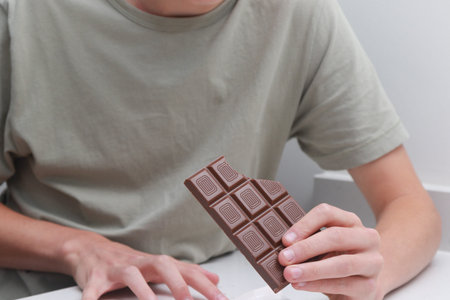 Teenage boy eating a bar of chocolate at a kitchen counter