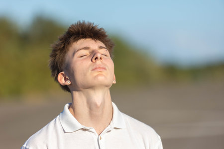 Portrait of a 17 year old boy in a white shirt and jeans,  outside on a warm summers afternoon with his eyes closed