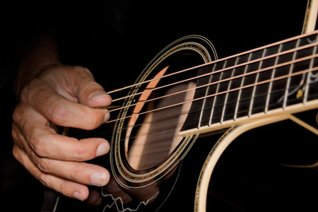 close-up of man playing a black acoustic guitar