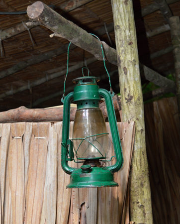 Green camping lantern hanging in front of a wooden hutの写真素材