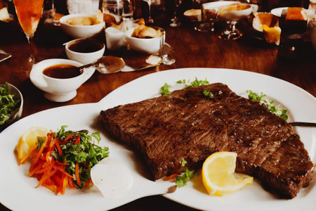 Delicious beef steak on a white plate with salad and lemon.の素材