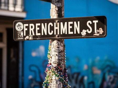 Frenchmen street sign with colorful beads and stickers in urban setting. That the image is generated using AI.の素材