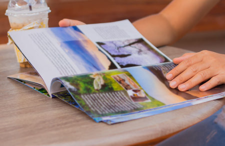 Female reading a magazine and drink ice coffee on wooden table.