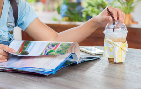 Female reading a magazine and drink ice coffee on wooden table.の写真素材