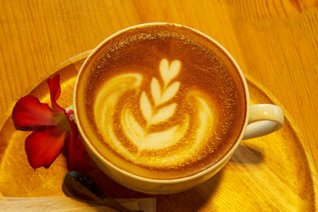 A cup of cafe latte and pink flower  with warm white light of  lamp, latte art coffee  with warm white light of  lamp in restaurant.の写真素材