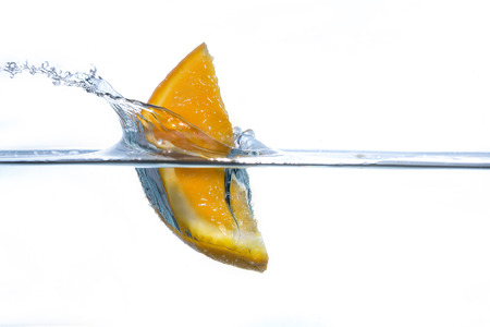 A piece of orange falling in waterの写真素材
