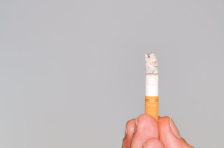 Closeup of a burning cigarette held between fingersの写真素材