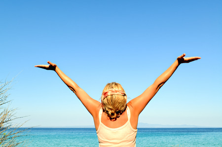Cheerful woman with arms raised to the sky near the seaの写真素材