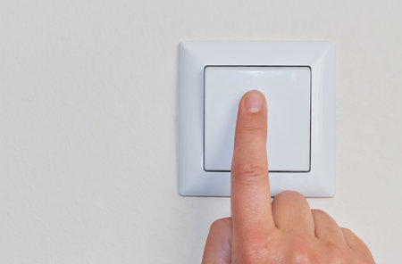 A hand of a woman pressing a wall mounted light switch