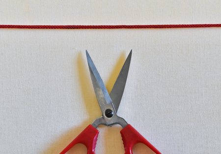 Closeup of scissors and red rope on bright textile backgroundの写真素材