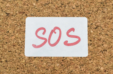 Word SOS handwritten on a sticker pinned on a cork board