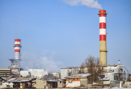 Chimney of a factory exhausting toxic and harmful smoke near a poor suburbの写真素材