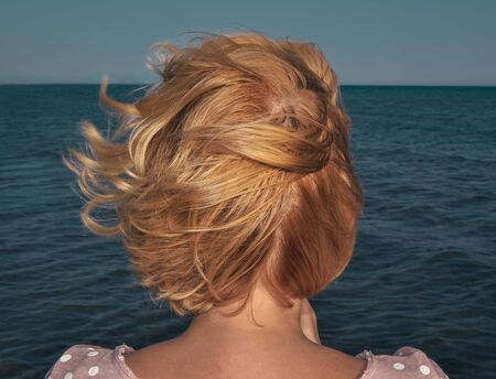 Woman with beautiful blond hair by the sea looking at the horizonの写真素材
