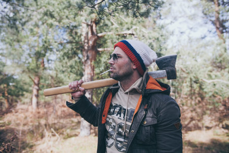 Handsome strong stylish man holding wooden axe in forest outdoor