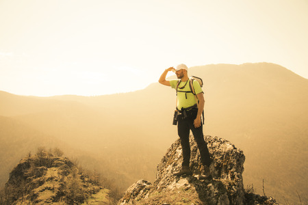 Successful young hiker standing on the top of the mountain and looking around.の写真素材