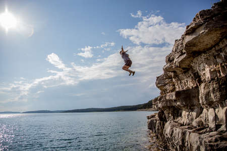A group of friends jump from cliffs into the lakeの写真素材