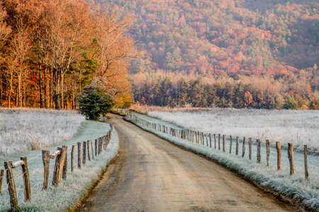 A gravel path leads through the valley with fields that have frosted from cold weather on both sides and mountians in the background の写真素材