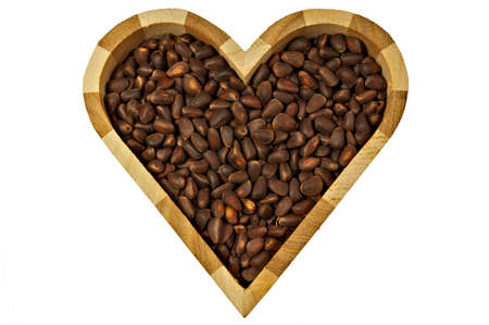 The wooden box in the shape of a heart with pine nuts inside, isolated on a white background, close-up.の写真素材