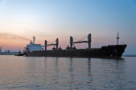 The ore carrier heaves out of the harbor on a tow, the photo is taken at sunset.の写真素材