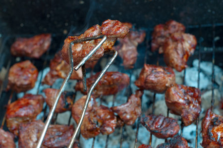 Meat on grill, a piece of meat in nippers  Closeup  