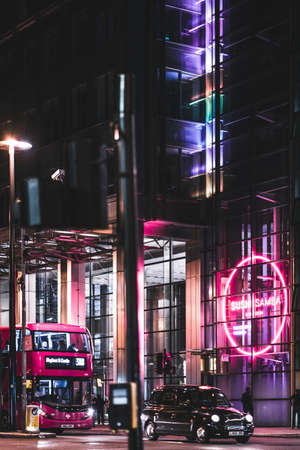 Bus and black cab in front of a neon sign in London at nightのeditorial素材
