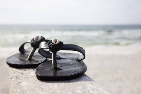 Black flip flops with shells on the beachの写真素材