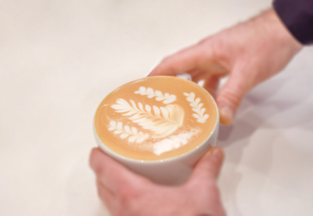 Fresh cup of cafe latte with milk latte art on white table in barista handsの写真素材
