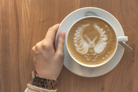 Girl holding a cup of fresh espresso cappuccino on a wooden table in a cafeの写真素材