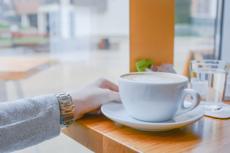 Girl holding big white cup of cafe latte in cafeteria on bright day