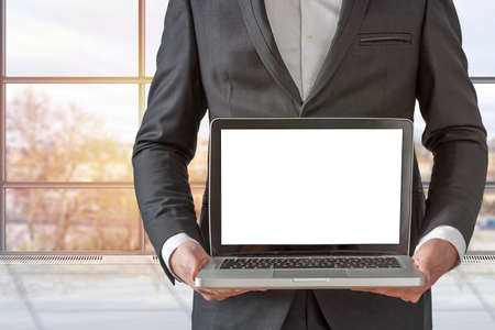 Businessman holding a computer and displaying the screen in the officeの写真素材