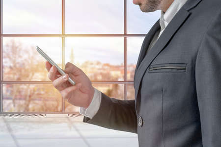 Male hands using modern mobile phone in the office with big windowの写真素材