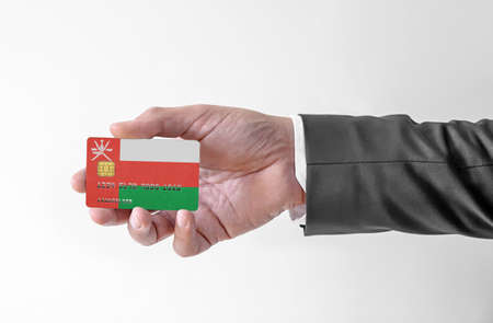 Bank credit plastic card with flag of Oman holding man in elegant suitの写真素材