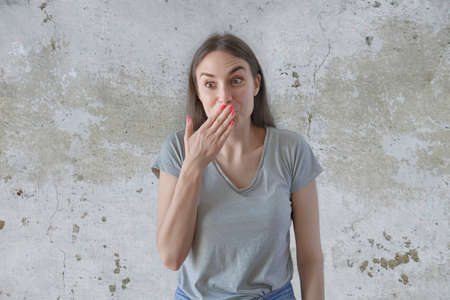 Pretty girl covering her mouth with hand and smiling over grey backgroundの写真素材