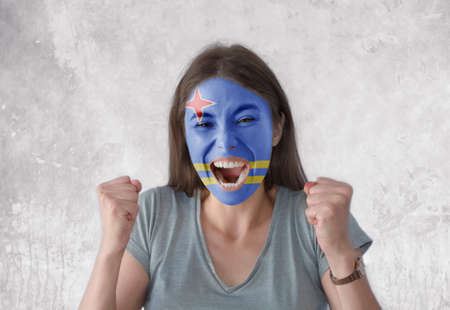 Young woman with painted flag of Aruba and open mouth looking energetic with fists upの写真素材