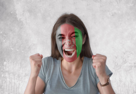 Young woman with painted flag of Afghanistan and open mouth looking energetic with fists up