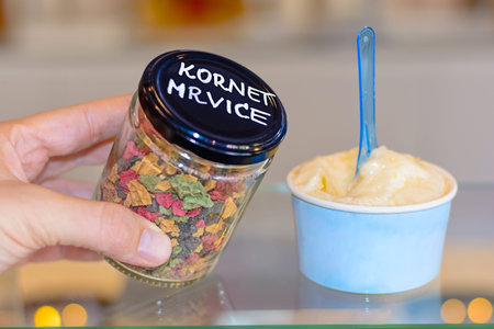 Hand holding jar and neapolitan ice cream scoops in blue cup on glass table