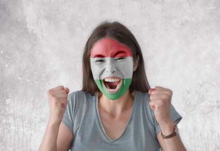 Young woman with painted flag of Hungary and open mouth looking energetic with fists upの写真素材