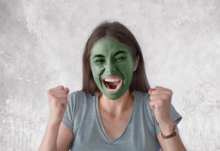 Young woman with painted flag of Gilgit Baltistan and open mouth looking energetic with fists upの写真素材