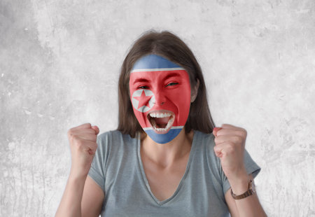 Young woman with painted flag of North Korea and open mouth looking energetic with fists upの写真素材