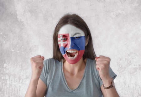 Young woman with painted flag of Slovakia and open mouth looking energetic with fists upの写真素材