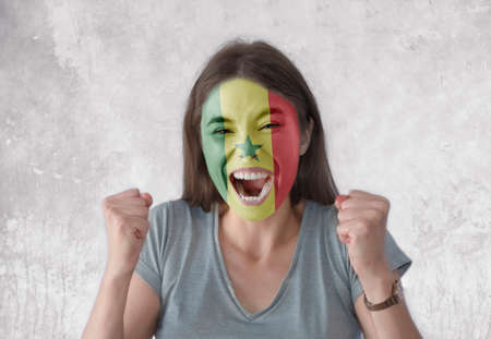 Young woman with painted flag of Senegal and open mouth looking energetic with fists upの写真素材