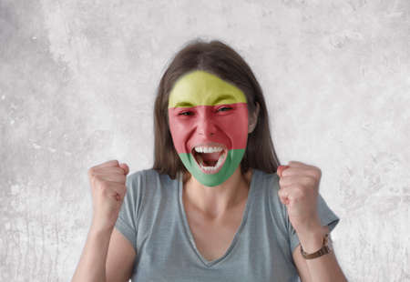 Young woman with painted flag of Syrian Kurdistan and open mouth looking energetic with fists upの写真素材