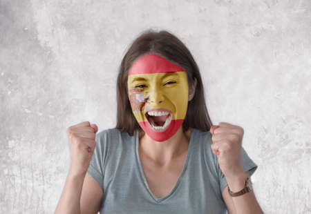 Young woman with painted flag of Spain and open mouth looking energetic with fists upの写真素材
