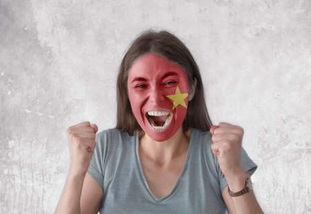Young woman with painted flag of Vietnam and open mouth looking energetic with fists upの写真素材
