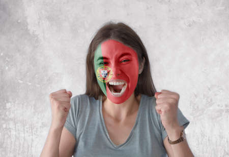 Young woman with painted flag of Portugal and open mouth looking energetic with fists upの写真素材